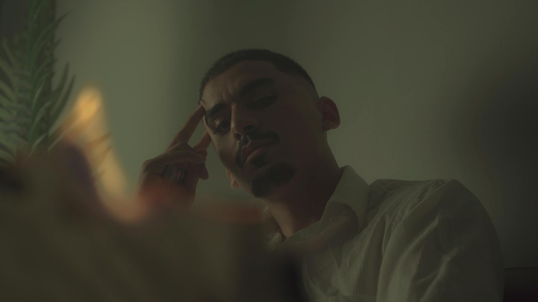 A contemplative man indoors with dramatic, moody lighting and a cinematic feel.